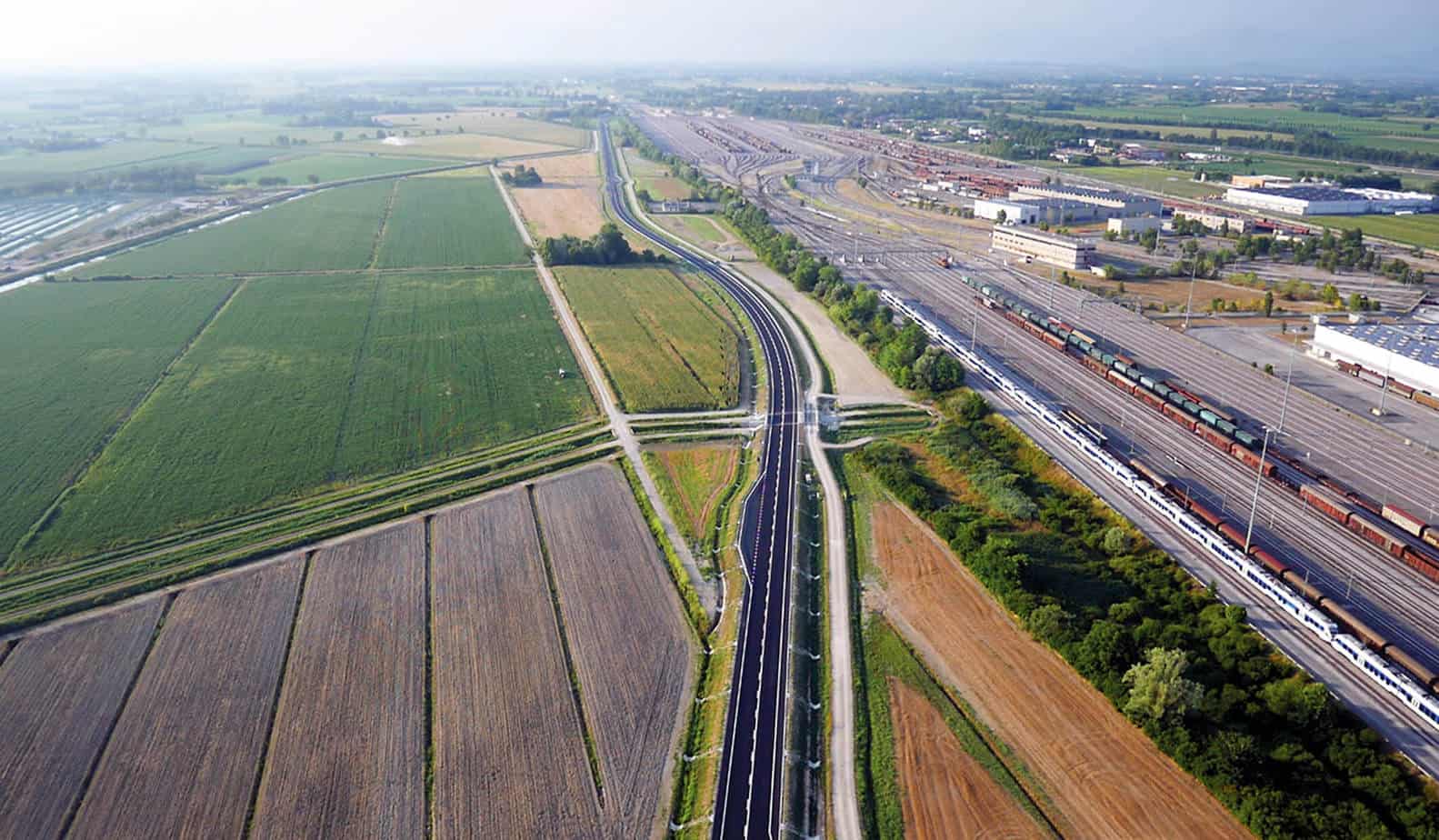 L’immagine dell’arteria stradale in prossimità dell’interporto ferroviario di Cervignano. In primo piano, un ponte delle opere minori su canale consortile